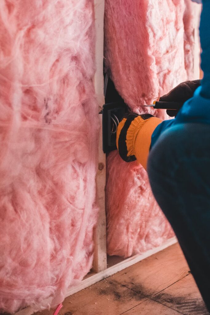 Focused worker installing pink fiberglass insulation in a building interior.